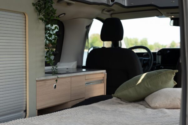 Der Innenraum des Smarttourer Camper Vans. Die ausgeklappte Smartbench verwandelt das Innere des Campers im Handumdrehen in ein gemütliches Schlafzimmer. Auf der Liegefläche liegt eine Decke und zwei weiche Kissen.