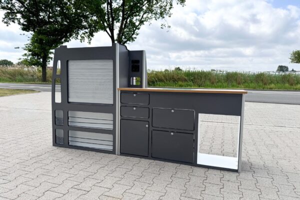 Das Smartkit Leichtbaumöbelset für den Selbstausbau des eigenen Camper Vans. Graue Fronten mit Schubladen und Schränken. Eine Arbeitsplatte in Holzoptik. Außerdem gibt es Aussparungen für den Kühlschrank und das Spülbecken.