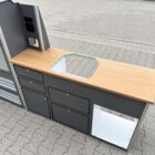 Das Smartkit Leichtbaumöbelset für den Selbstausbau des eigenen Camper Vans. Graue Fronten mit Schubladen und Schränken. Eine Arbeitsplatte in Holzoptik. Außerdem gibt es Aussparungen für den Kühlschrank und das Spülbecken.
