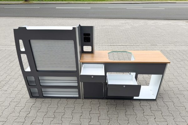 Das Smartkit Leichtbaumöbelset für den Selbstausbau des eigenen Camper Vans. Graue Fronten mit Schubladen und Schränken. Eine Arbeitsplatte in Holzoptik. Außerdem gibt es Aussparungen für den Kühlschrank und das Spülbecken.