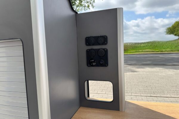 Das Smartkit Leichtbaumöbelset für den Selbstausbau des eigenen Camper Vans. Graue Fronten mit Schubladen und Schränken. Eine Arbeitsplatte in Holzoptik. Es gibt bereits verbaute Elektroanschlüsse.